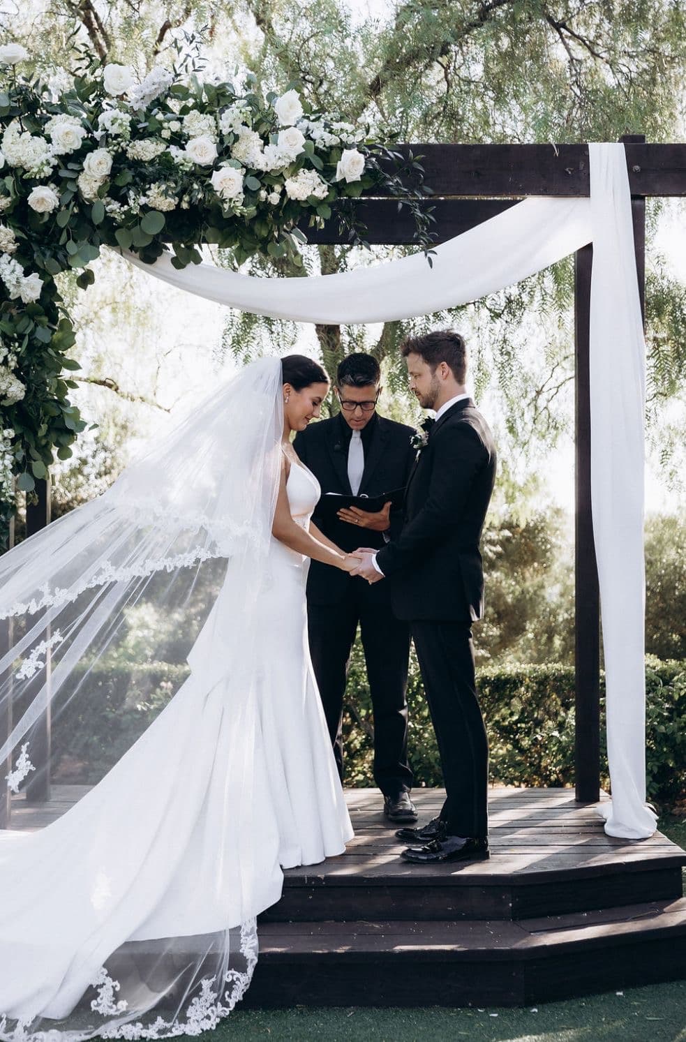 Ceremony moment under floral arch with white draping