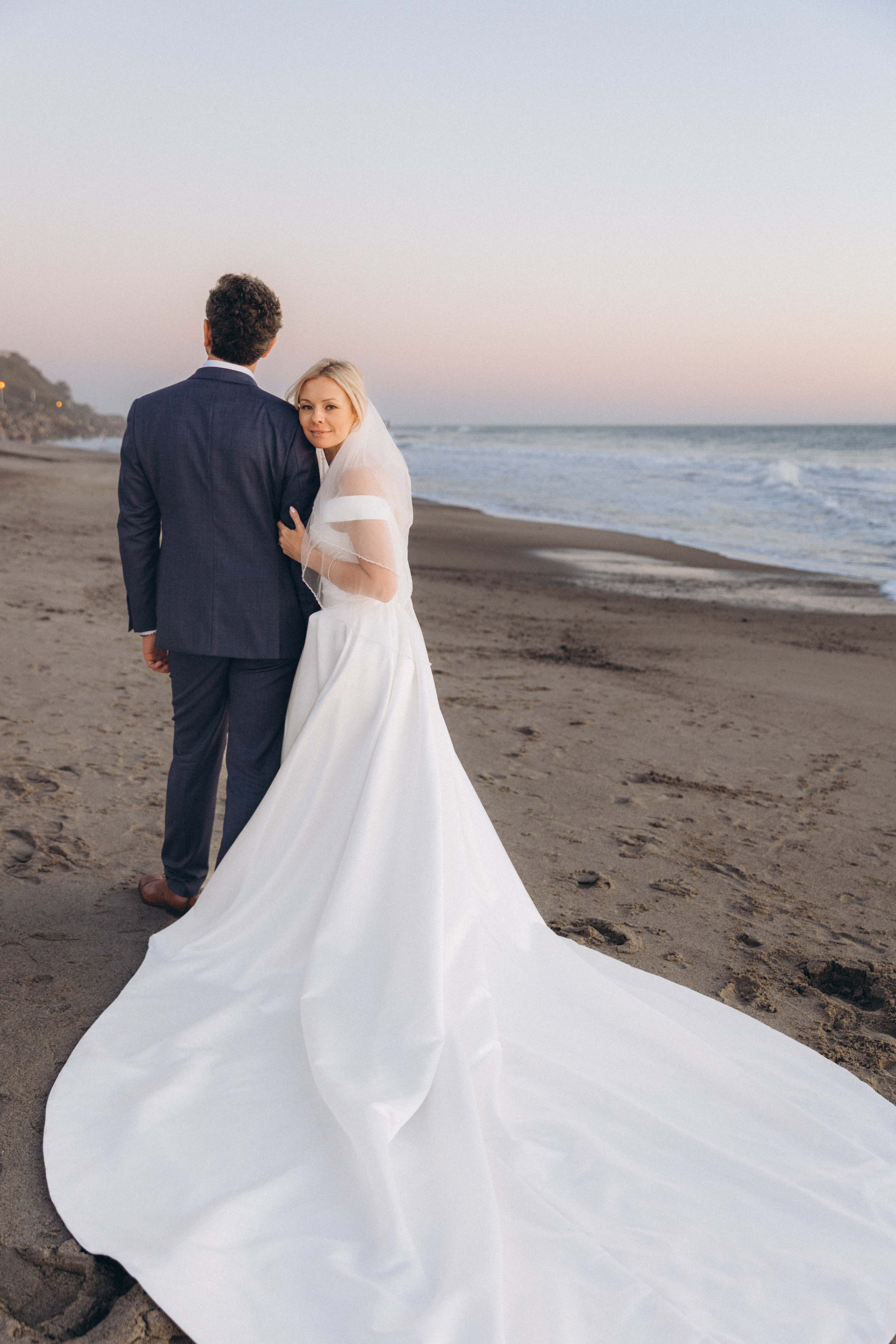 Bride looking back on beach with long train