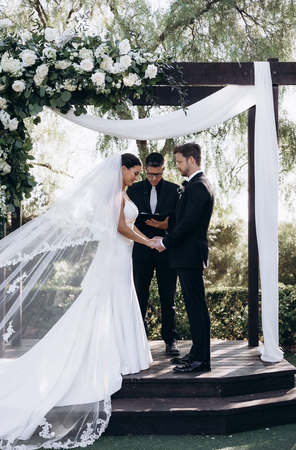 Ceremony moment under floral arch with white draping