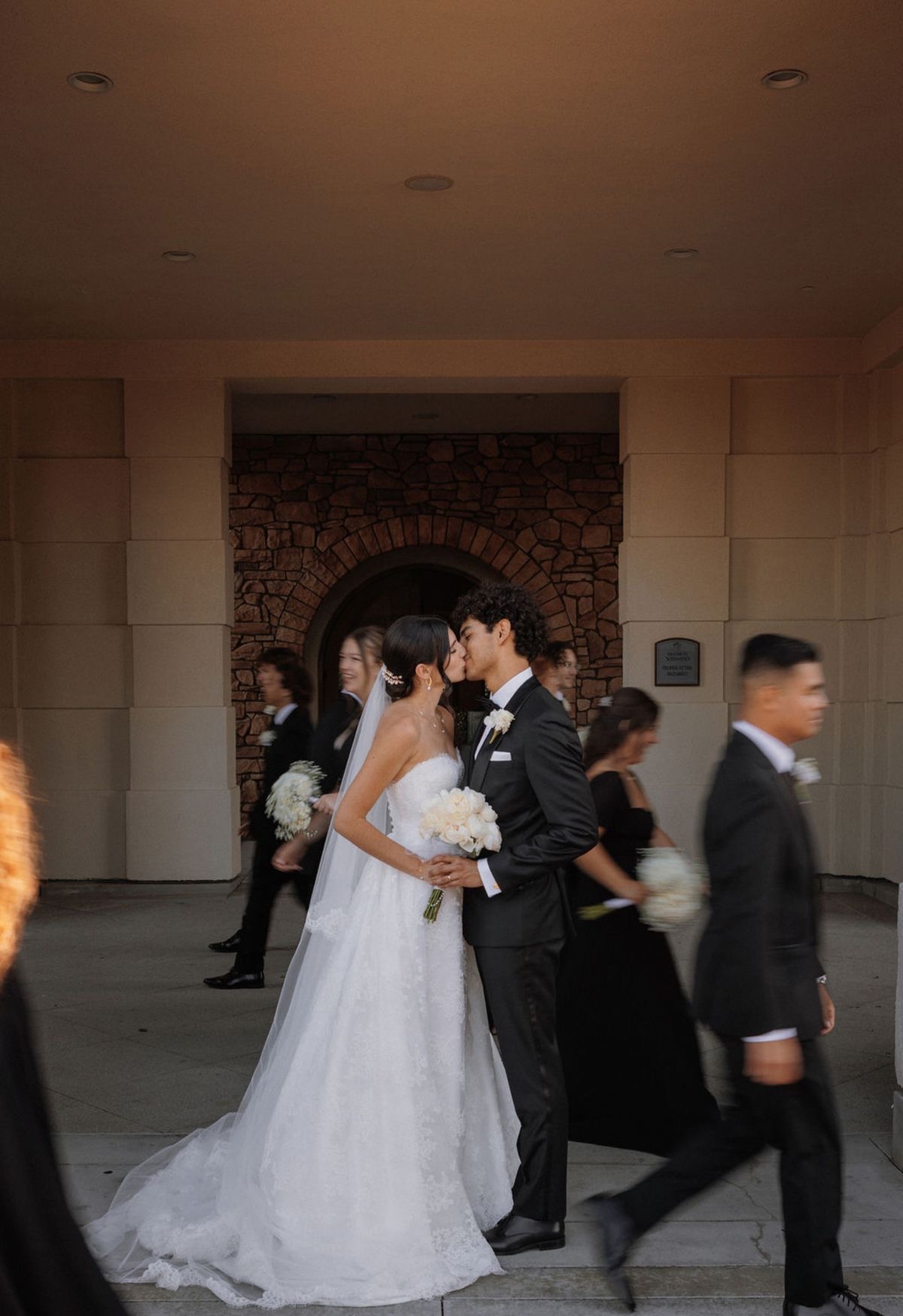 Couple kissing with wedding party in motion blur