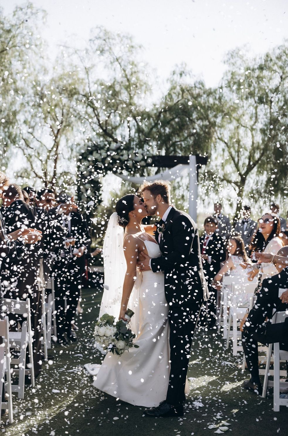 Couple kissing with confetti at outdoor ceremony