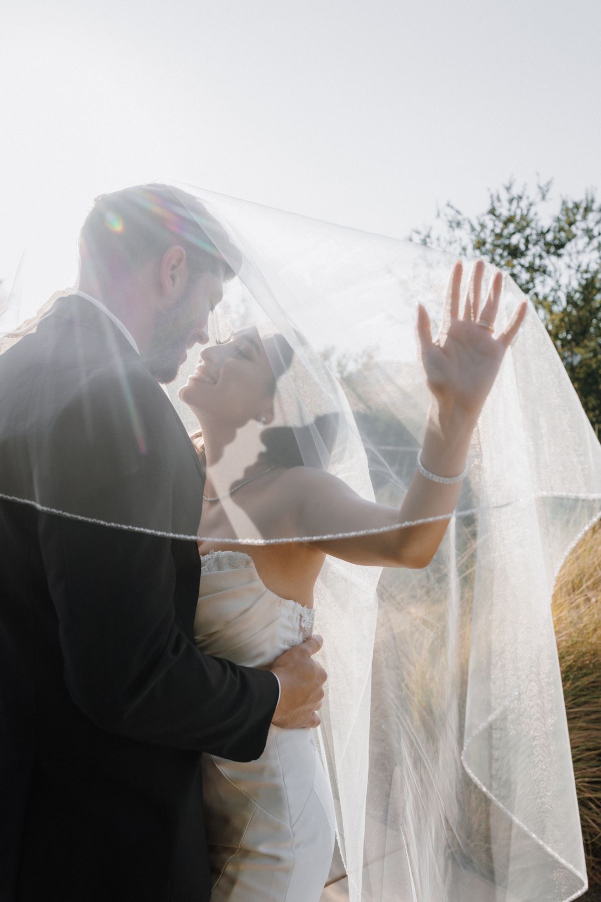 Couple under flowing veil with sun flare