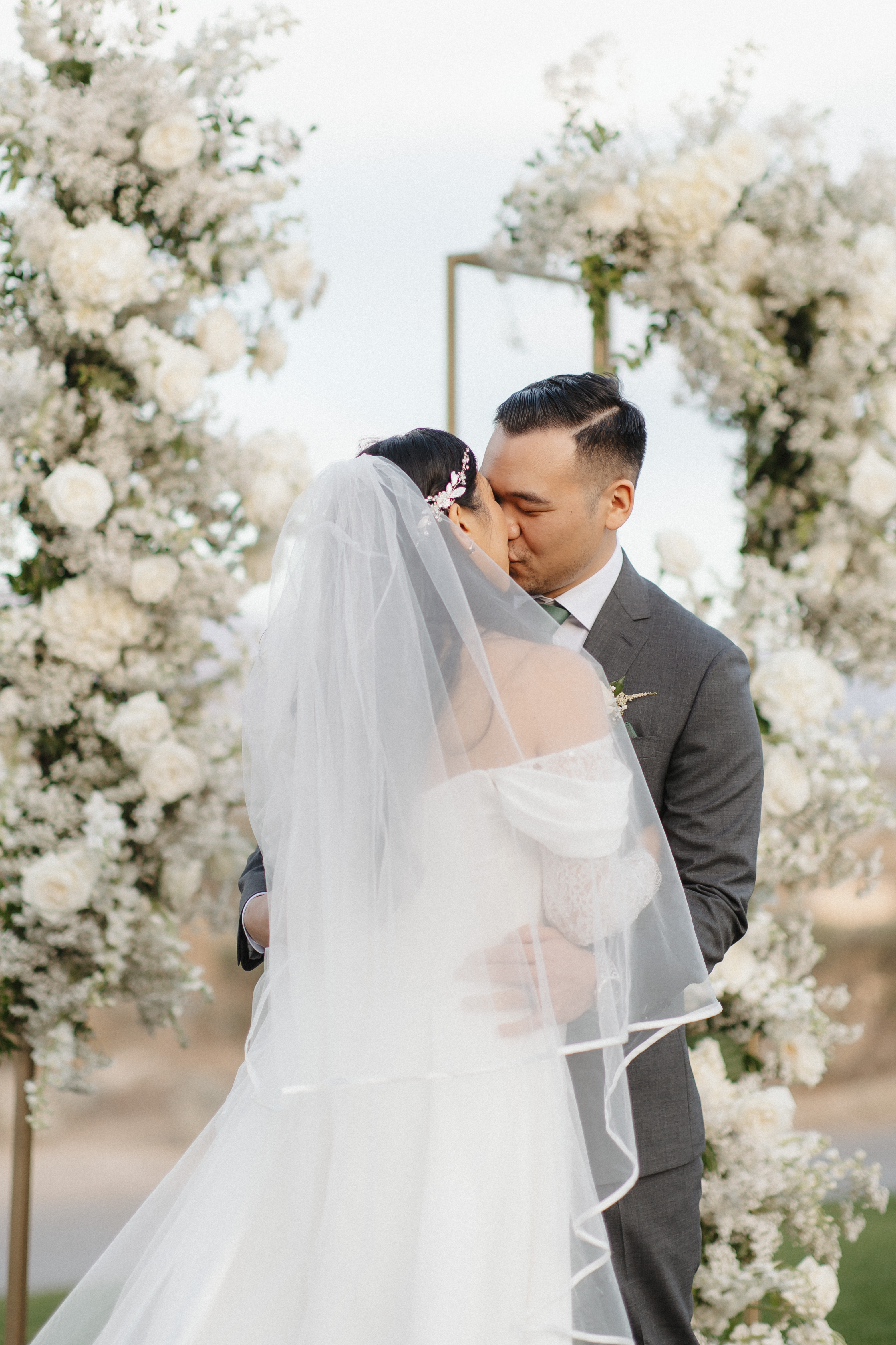Ceremony kiss under white floral arch